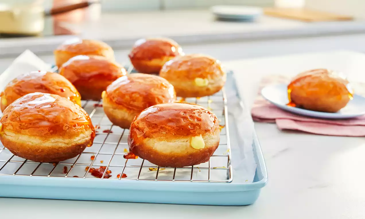 Golden round doughnuts with glossy caramel tops and rich cream filling on a cooling rack and plate against a bright kitchen background