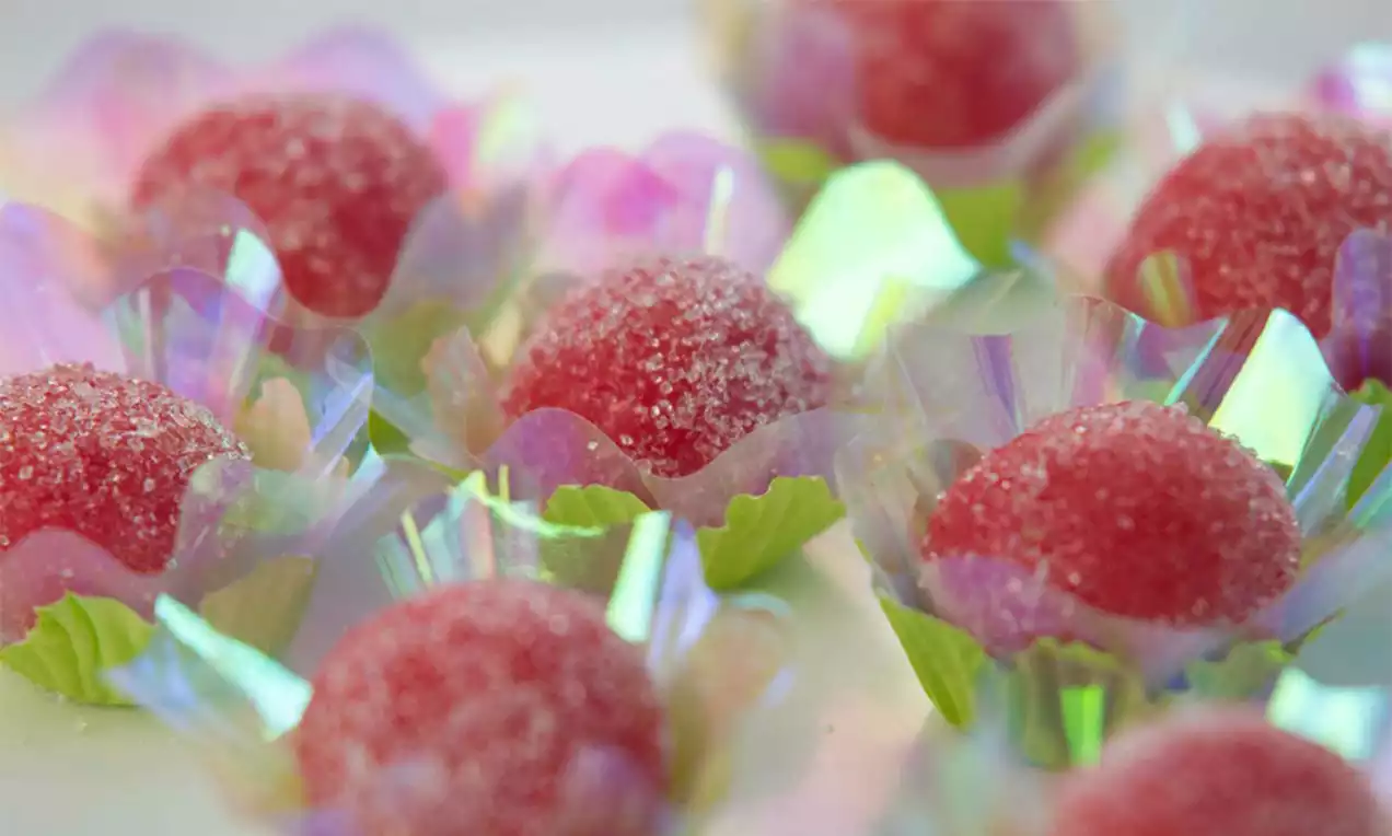 Brigadeiros vermelhos com superfície açucarada e cintilante em formas de papel holográfico com base verde sobre fundo claro