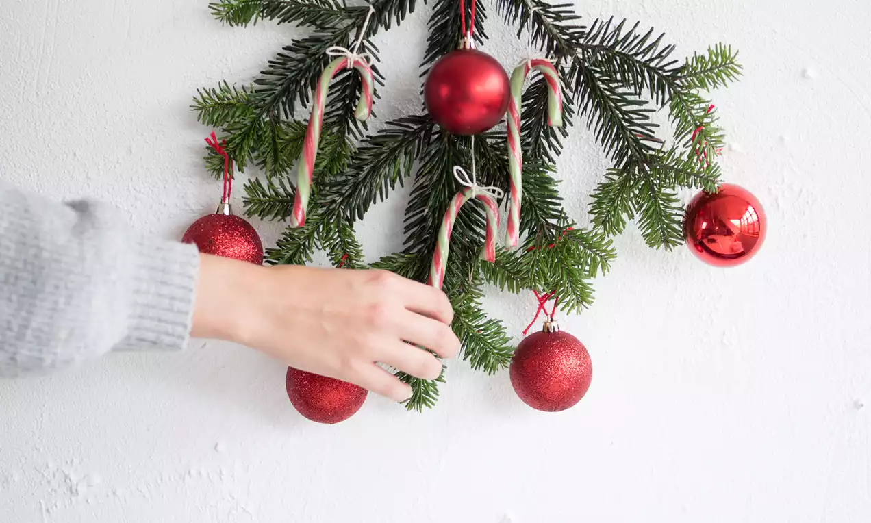 Pebermyntestokke med røde og hvide spiralstriber hænger på grønne grangrene sammen med røde matte og skinnende kugler