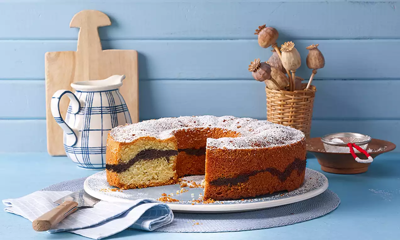 Altdeutscher Mohnkuchen mit goldbrauner Kruste, Mohnfüllung in welliger Schichtung, bestäubt mit Puderzucker auf weißem Teller