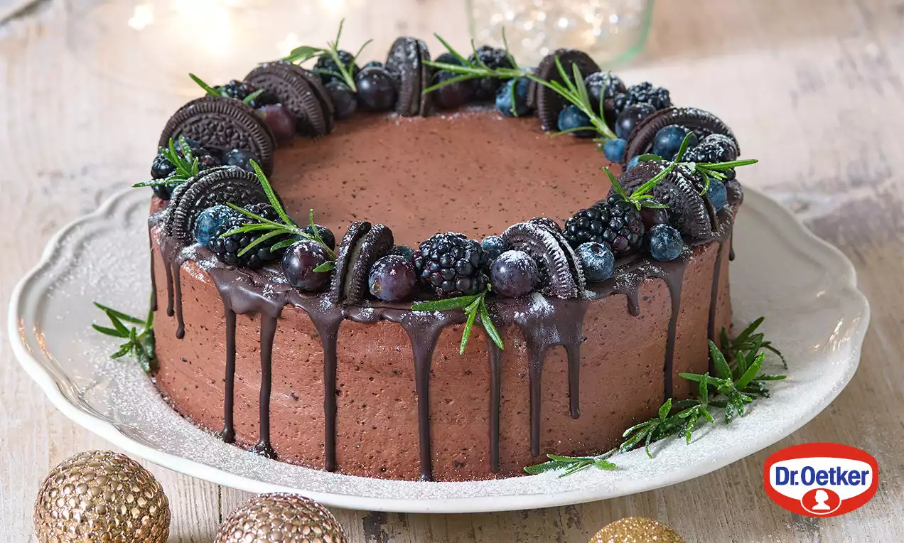Dvoubarevný čokoládový dort s lesklou ganache, zdobený ostružinami, borůvkami, sušenkami a snítkami zelené na světle zdobeném talíři