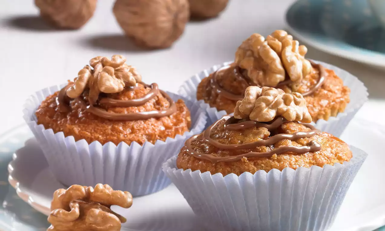 Walnuss-Schoko-Muffins in blauen Papierförmchen, goldbraun und weich, mit Walnusskern und Schokoglasur auf einem weißen Teller