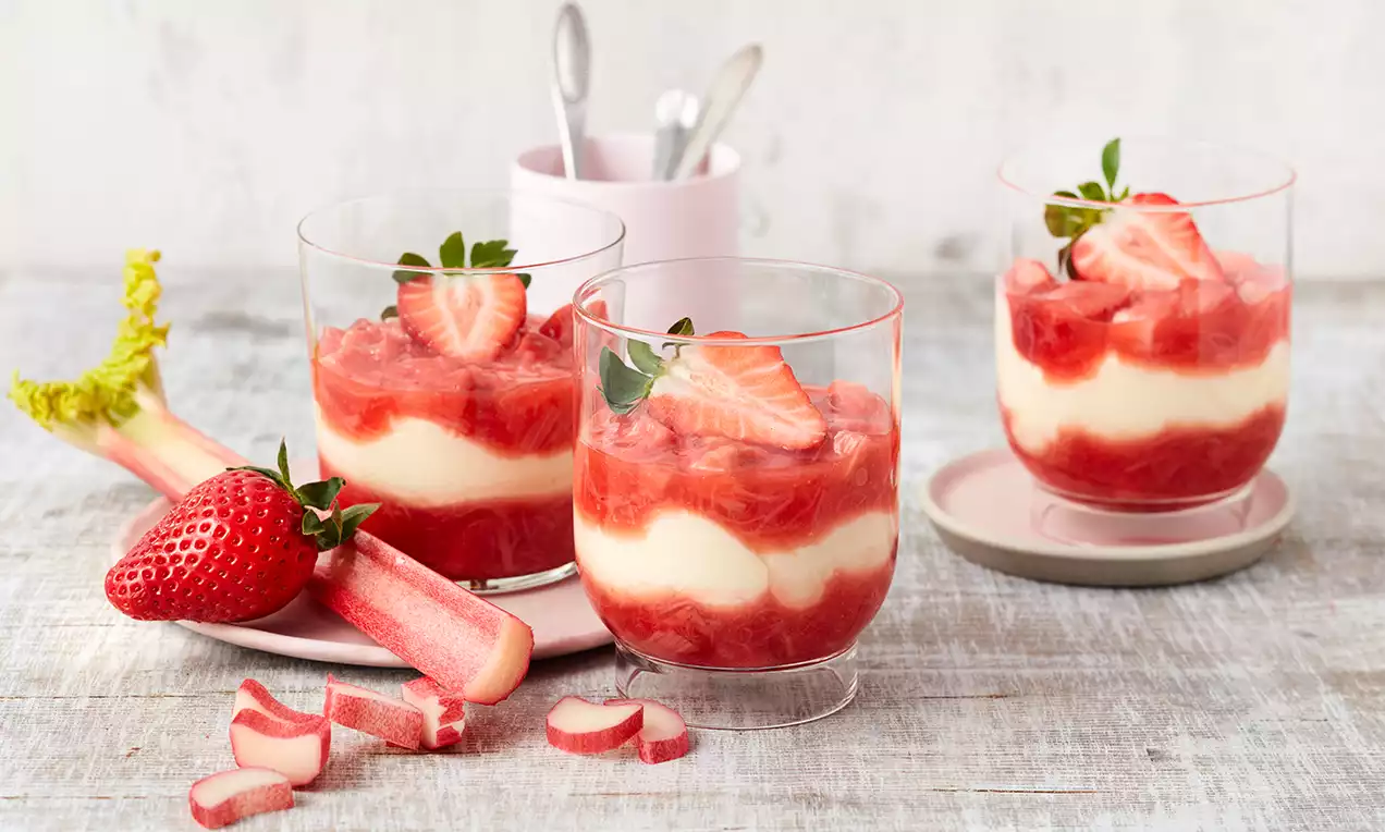Erdbeer-Rhabarber-Dessert in Gläsern mit Schichten aus weißer Creme und rot glänzendem Kompott, dekoriert mit frischen Erdbeeren und Blättchen