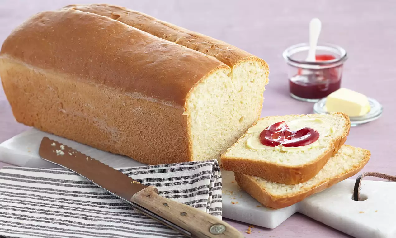 Quarkbrot mit Backpulver als goldbraunes Kastenbrot mit hellen, weichen Scheiben, auf Holzbrett serviert mit Butter und frischen Kräutern