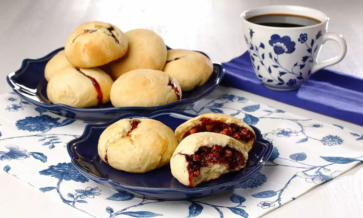 Altın sarısı pofuduk hamurlar, kırmızı marmelat dolgusuyla dolgun, lacivert tabaklarda sergilenmiş, yanında çiçekli bir fincan kahve