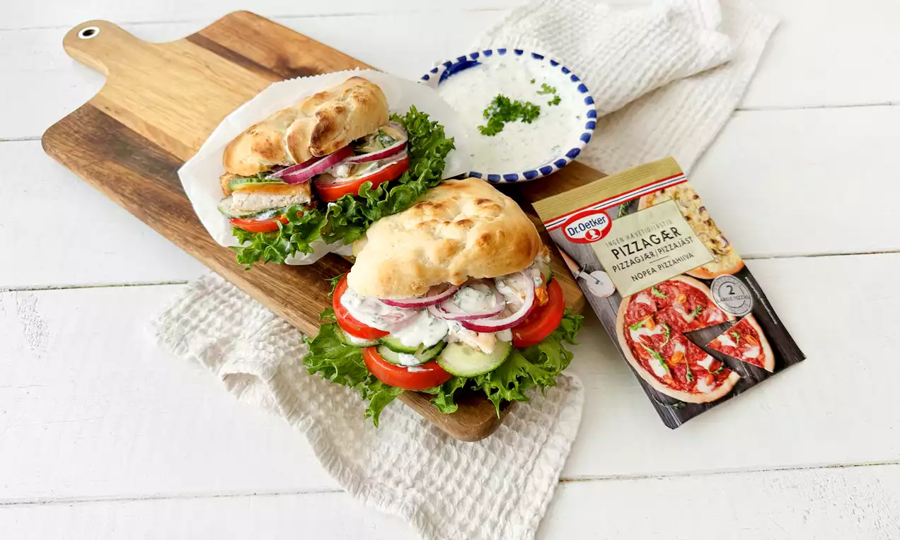 Kuohkeat pitaleivät täytettyinä tuoreilla vihanneksilla ja kermaisella kastikkeella, aseteltuina puiselle leikkuulaudalle valkoisen keittiöliinan päällä