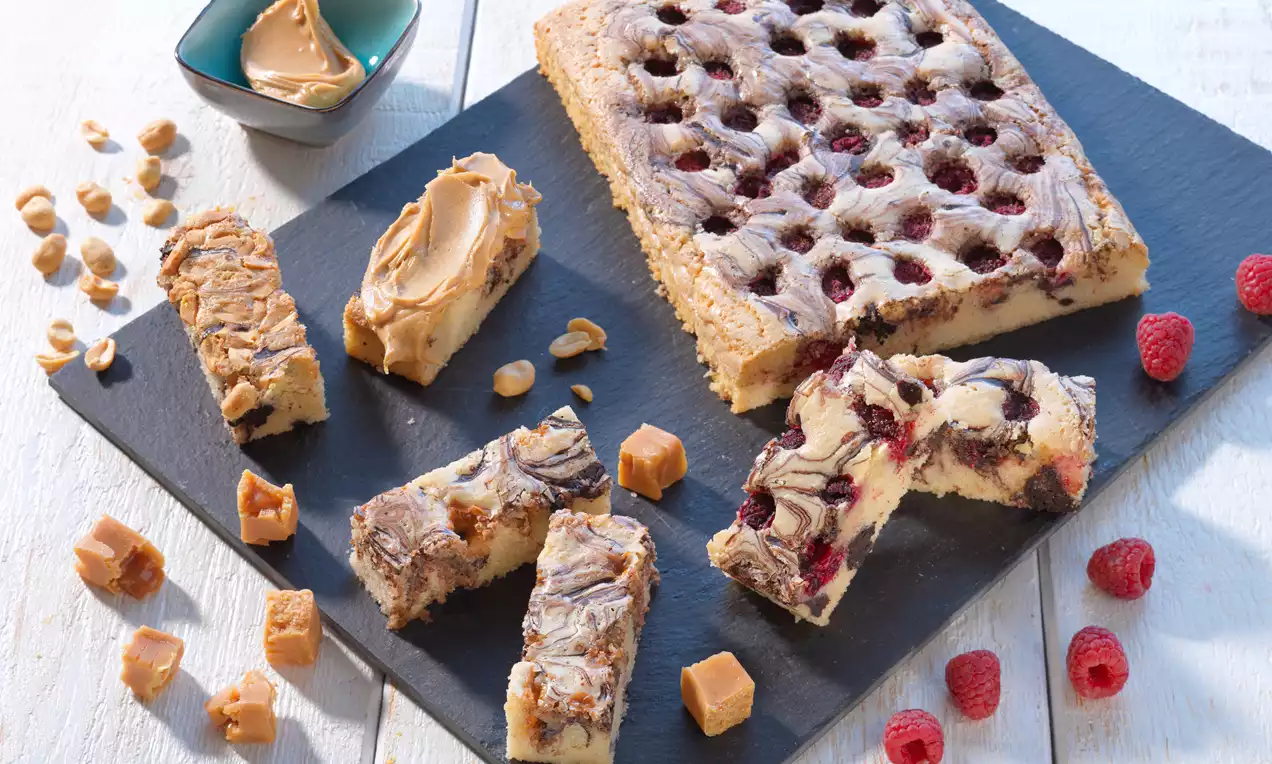 Marmor-Brownies mit heller und dunkler Teigstruktur, Himbeeren und Karamellstücke auf schwarzer Schieferplatte, daneben frische Himbeeren