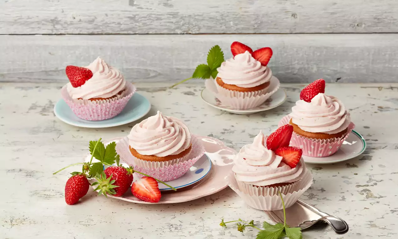 Erdbeer-Cupcakes aus hellem Mandelteig mit zartem rosa Erdbeer-Quark-Sahne-Topping, frischen Erdbeerstücken und Minzblatt