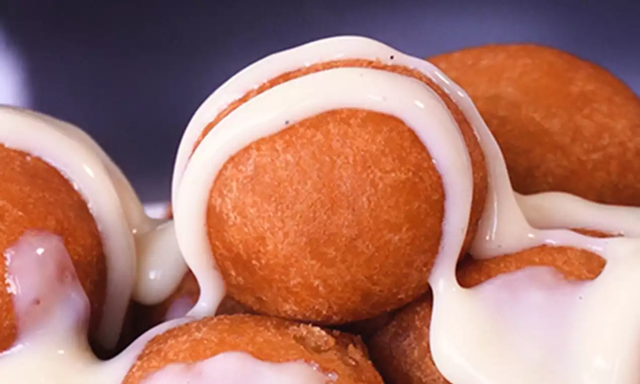 Male, zlatnosmeđe fritule okruglog oblika prelivene svijetložutom kremom, raspoređene u bijeloj posudi s glatkim rubovima