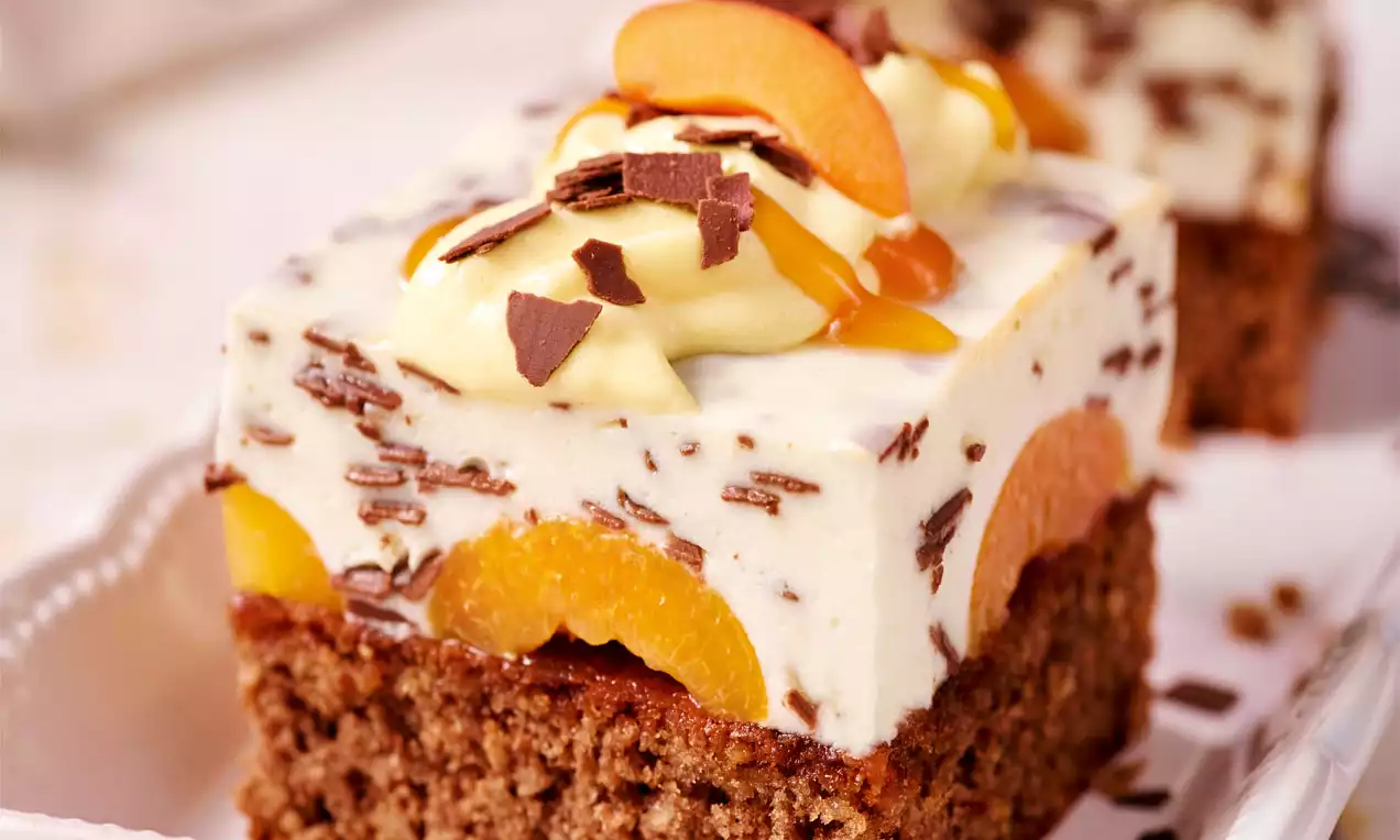 Stracciatella-Marillen-Schnitte mit braunem Schokobiskuitboden, heller Creme, eingebackenen Aprikosenscheiben und Schokostreuseln dekoriert