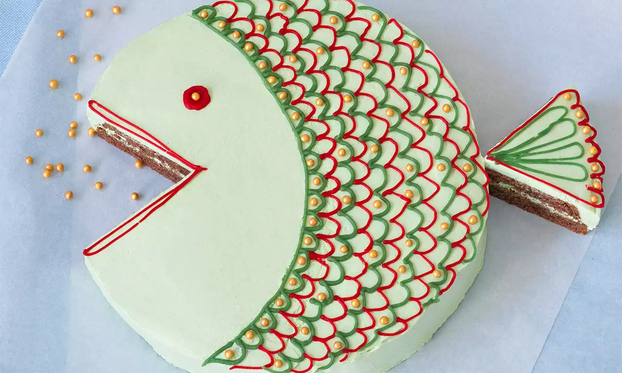 Kruhovo tvarovaná torta svetlozelenej farby s červenými a zelenými vzormi pripomínajúcimi šupiny, doplnená o trojuholníkový chvost a zlaté dekorácie