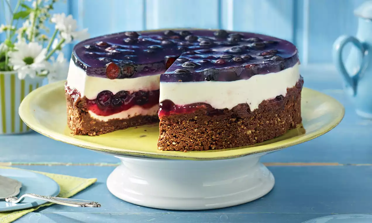 Kleine Heidelbeer-Joghurt-Torte mit knusprigem braunem Boden, weißer Joghurtfüllung und glänzendem Heidelbeerspiegel auf einer gelben Platte