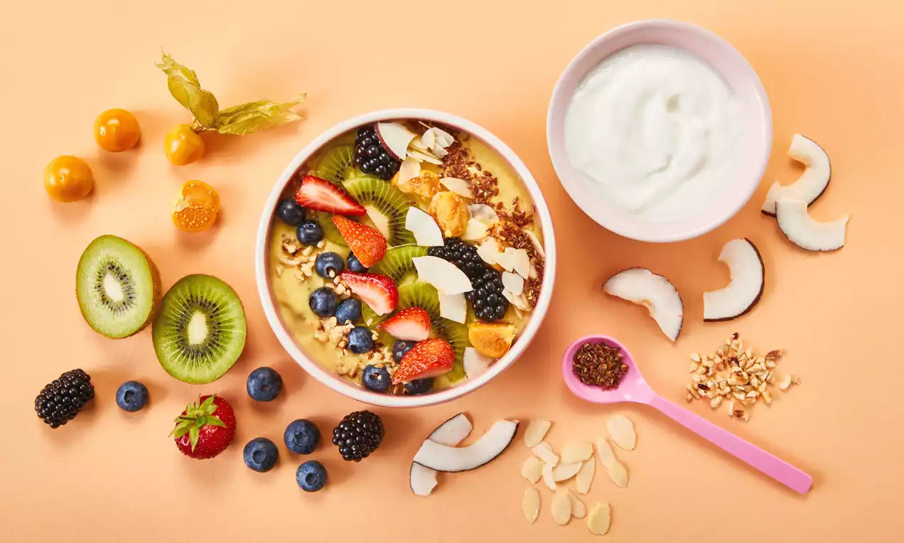 Sunshine Smoothie Bowl mit leuchtend buntem Obst wie Kiwi, Beeren und Physalis, Granola und Kokosstücken, serviert in weißer Schale auf hellem Untergrund