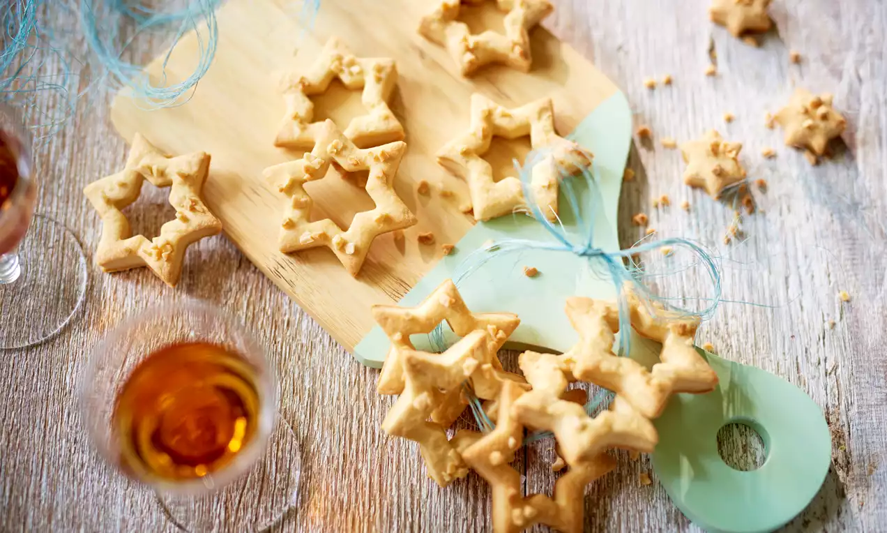 Gwiazdkowe ciasteczka w złocistym odcieniu, delikatnie chrupiące, ułożone na drewnianej desce i ozdobione błękitnymi wstążkami