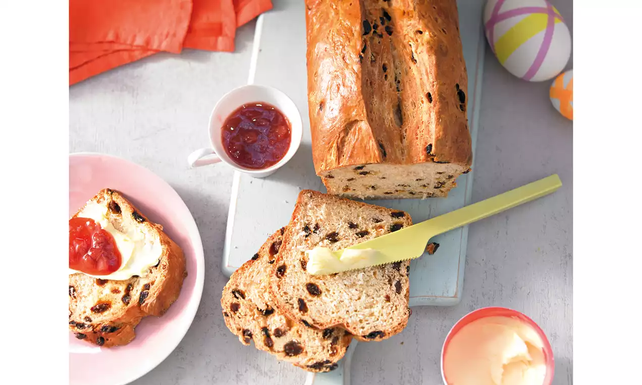Rosinen-Butter-Stuten mit goldbrauner Kruste, weichen Scheiben voller dunkler Rosinen, gelbem Messer, serviert mit Marmelade und Butter