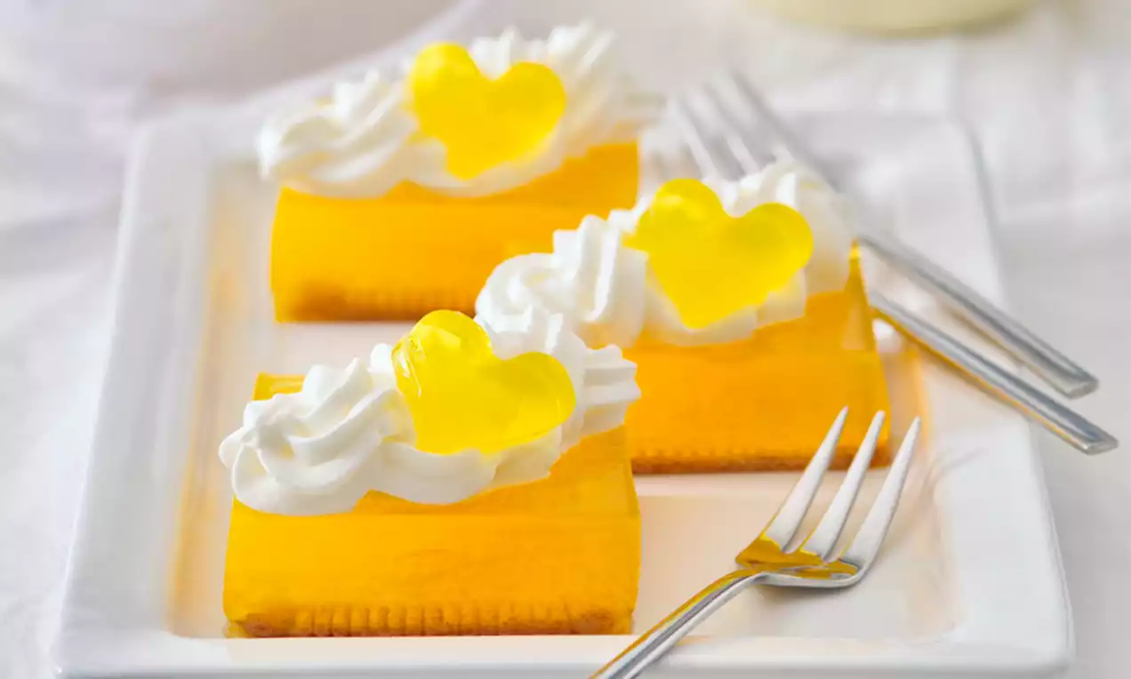 Čiré želé ve tvaru srdíček na proužcích jasně žlutého želé, ozdobené nadýchanými šlehačkovými spirálami na bílém čtvercovém talíři