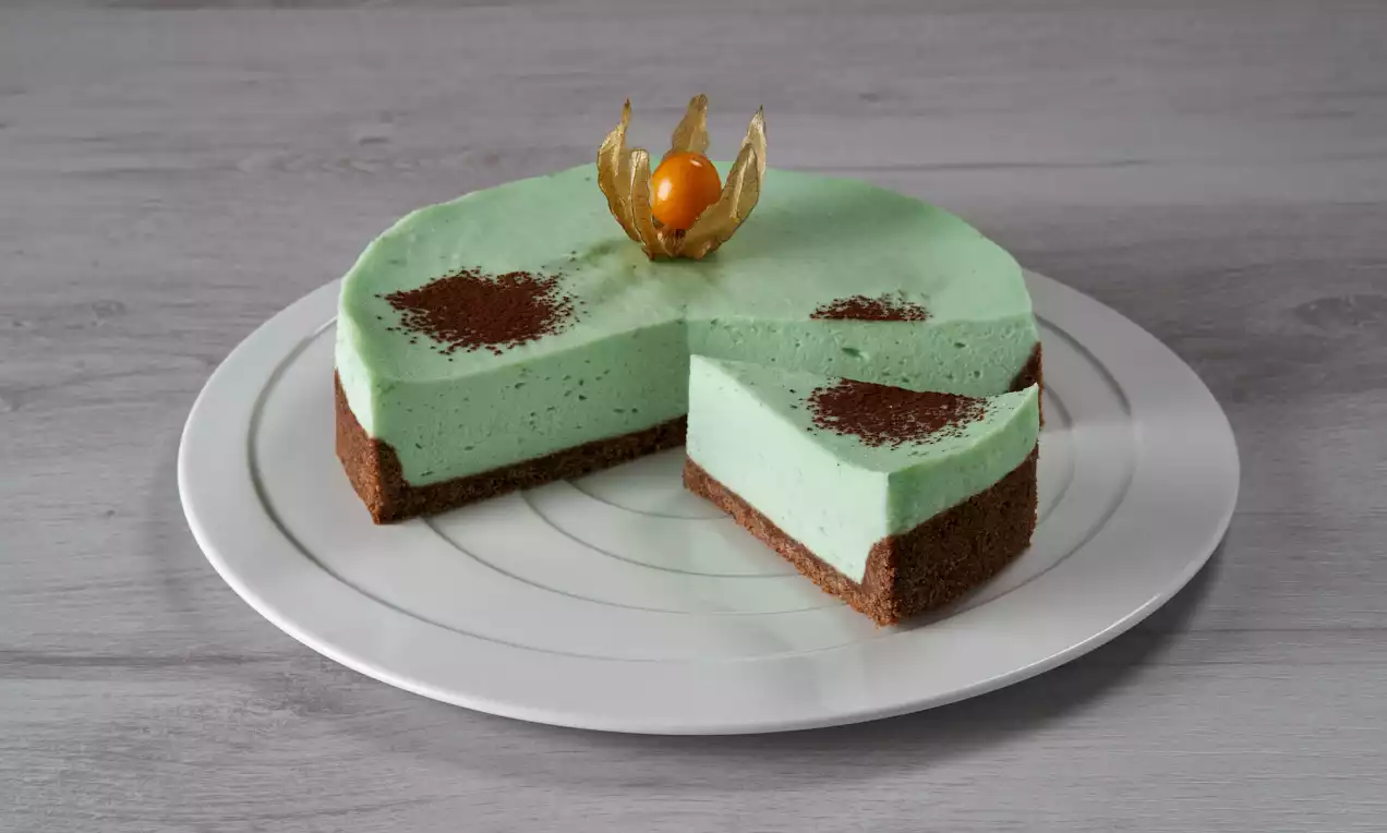 Torta bavarese verde menta su base marrone di pan di spagna, decorata con polvere di cacao e un alchechengi dorato al centro