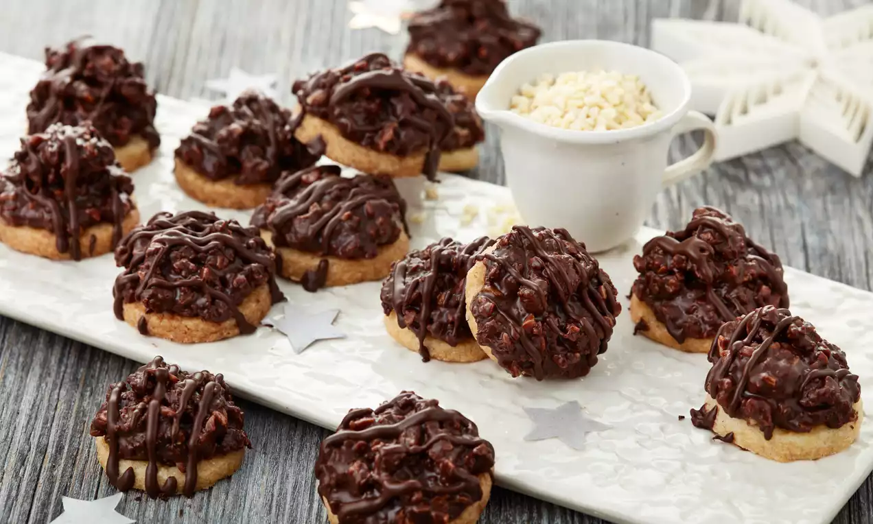 Granatsplitter aus dunkler Schokoladenkuppel mit knusprigen Stückchen auf hellem Boden, arrangiert auf weißer Platte mit Stern-Dekoration