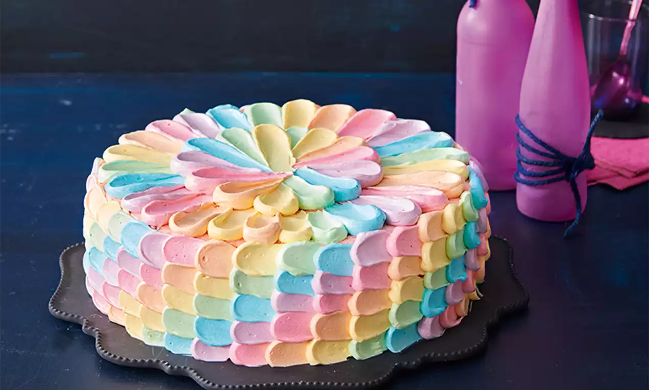 Regenbogen-Pink-Grapefruit-Torte mit geschwungener Creme in pastelligen Farben, schuppenartig dekoriert auf einer dunklen Tortenplatte