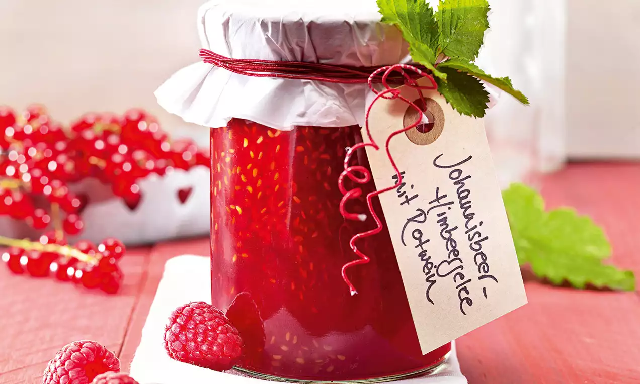 Confettura lucida rosso intenso con semi visibili in vasetto decorato con carta bianca, cordino rosso, etichetta e rametto di foglie verdi