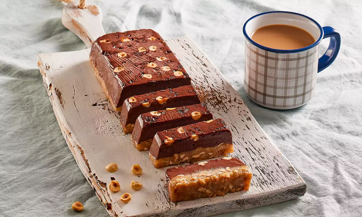 Dilimlenmiş supangleli muzlu parfait, üstü bütün fındıklarla süslenmiş, rustik beyaz ahşap üzerinde bir fincan çay eşliğinde