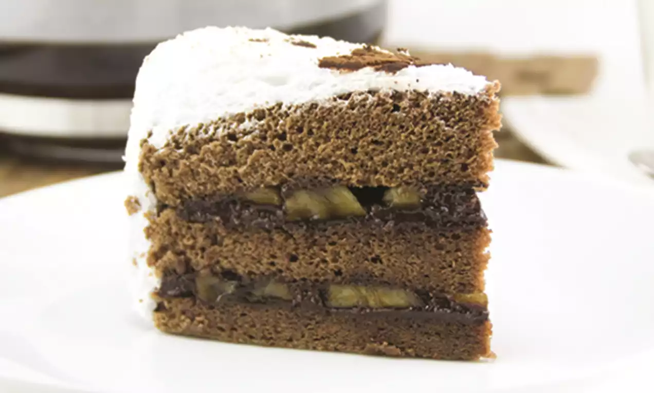 A slice of chocolate sponge cake layered with banana slices and dark chocolate filling, topped with white frosting and chocolate shavings