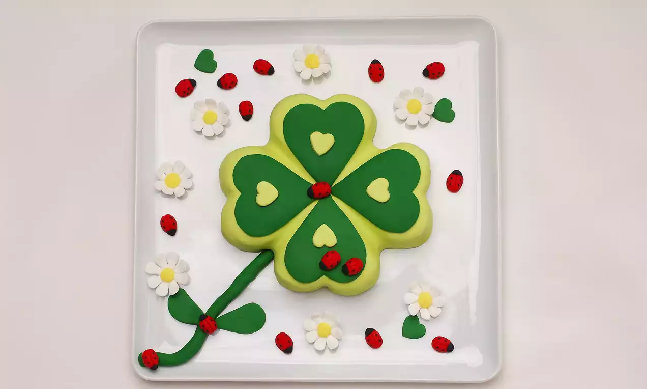 Yeşil yonca şeklinde şeker hamurlu pasta, yapraklarında sarı kalp desenler, yanında şekerden uğur böcekleri ve papatyalarla süslenmiş