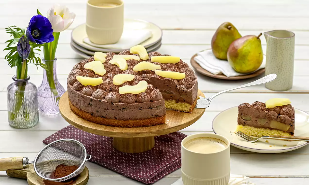 Schokoladentorte mit heller Birnenfüllung und Tupfen aus Mousse, belegt mit Birnenspalten, auf einer Holzplatte arrangiert
