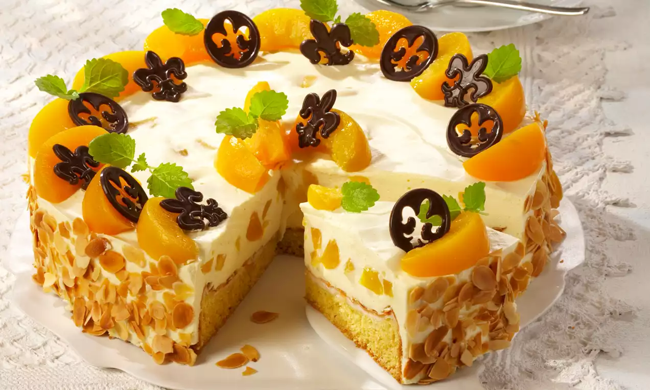 Beze torta s kremom boje vanilije, dekorirana kriškama breskve, listićima badema, čokoladnim ukrasima i listićima mente