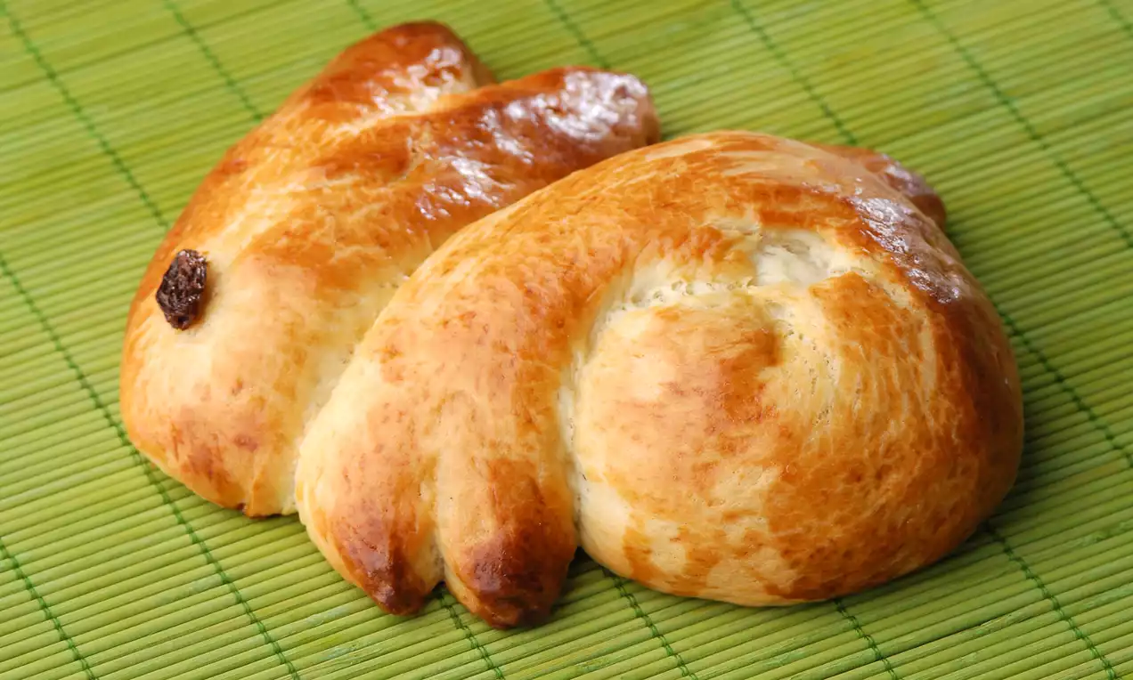 Altın rengi parlak yüzeyli, tavşan şeklinde biçimlendirilmiş hamur işleri, bir mat yeşil hasır zemin üzerinde bir arada duruyor