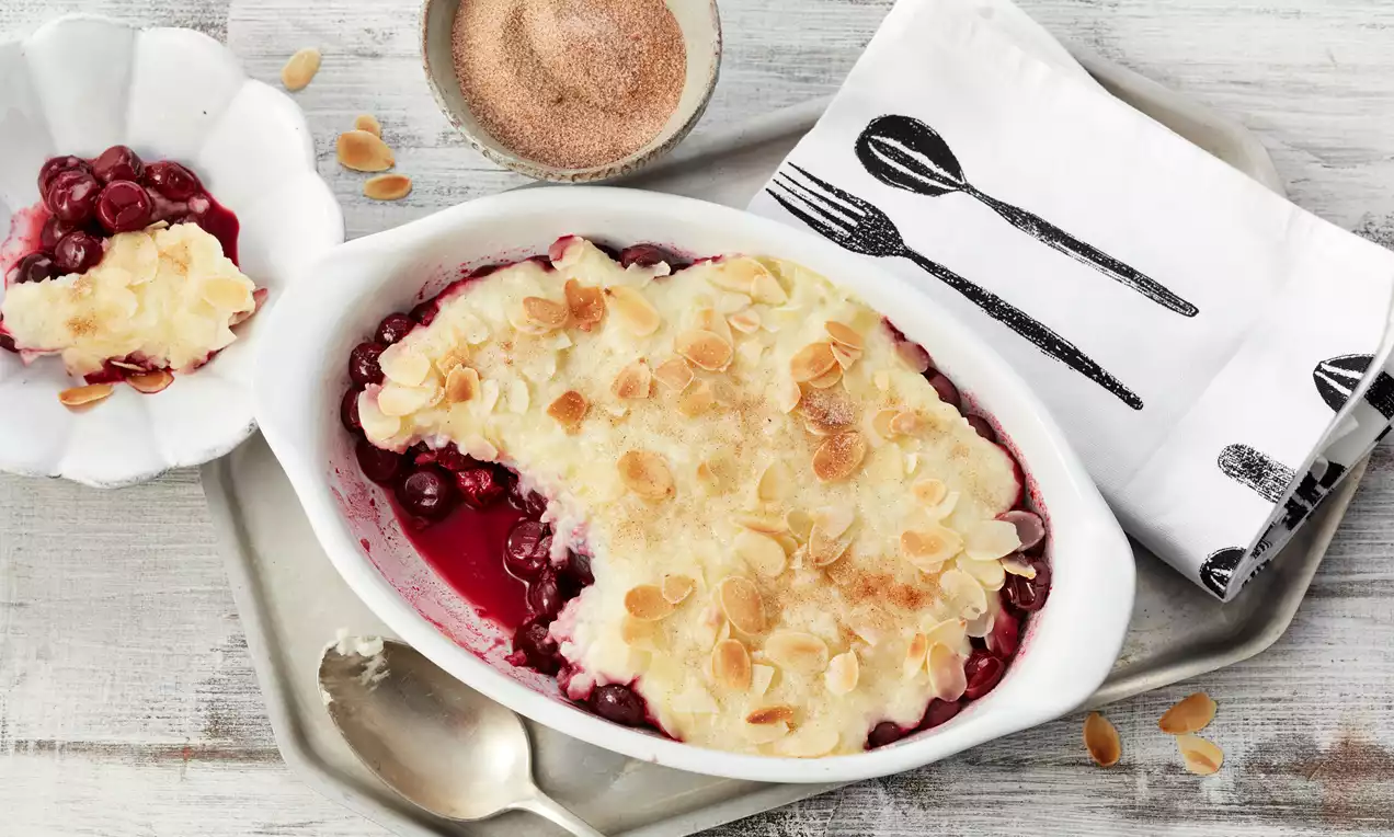Milchreis-Auflauf mit glänzenden roten Kirschen, goldbrauner gratinierter Oberfläche, serviert in weißer Auflaufform mit Minzblättern