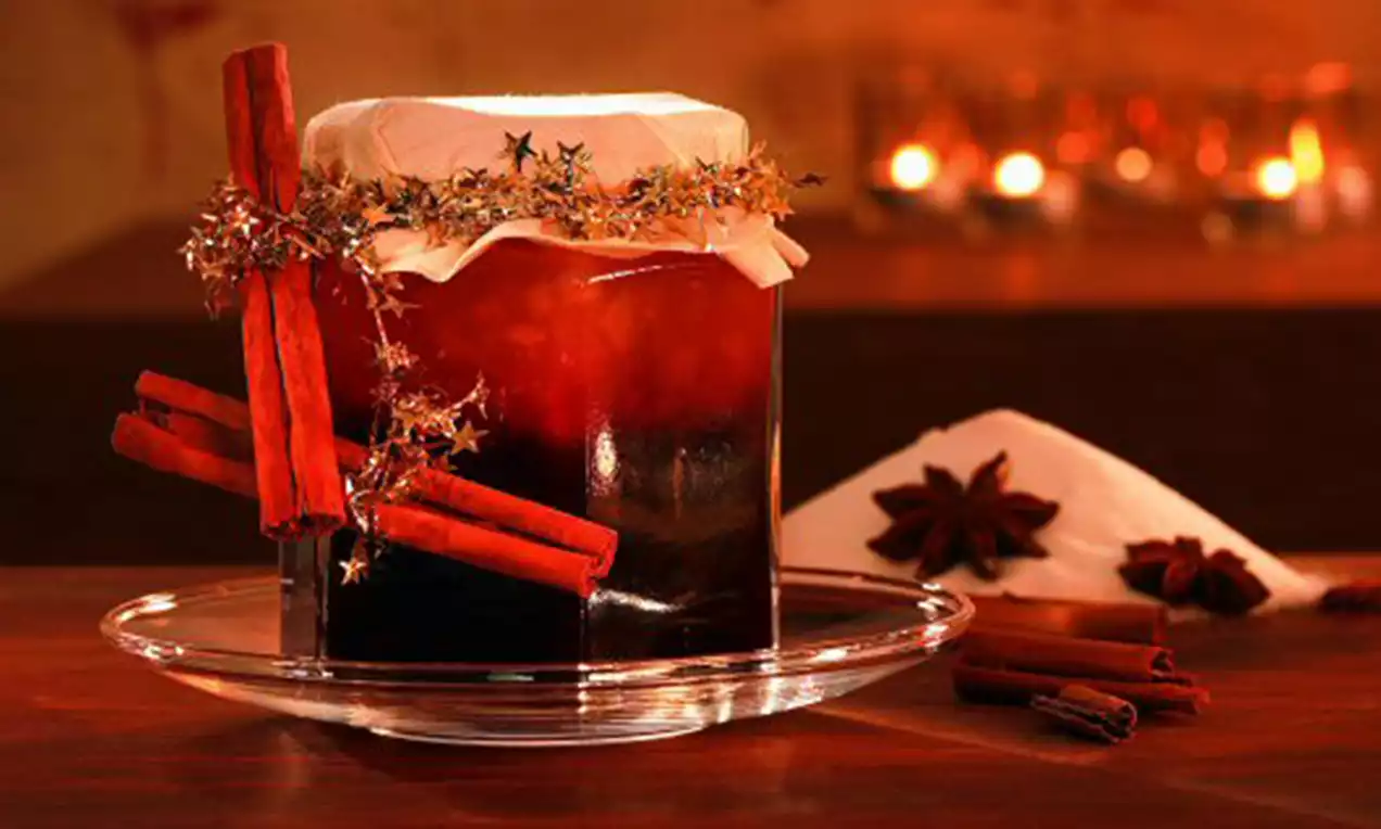 Dieprode kerstconfituur in een glazen pot met wit papier en sterrenlint, gedecoreerd met kaneelstokjes op een glazen schotel, omringd door steranijs