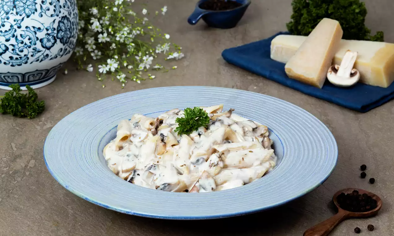 Creamy mushroom pasta with light brown penne and tender mushroom slices in white sauce, garnished with fresh parsley on a blue plate