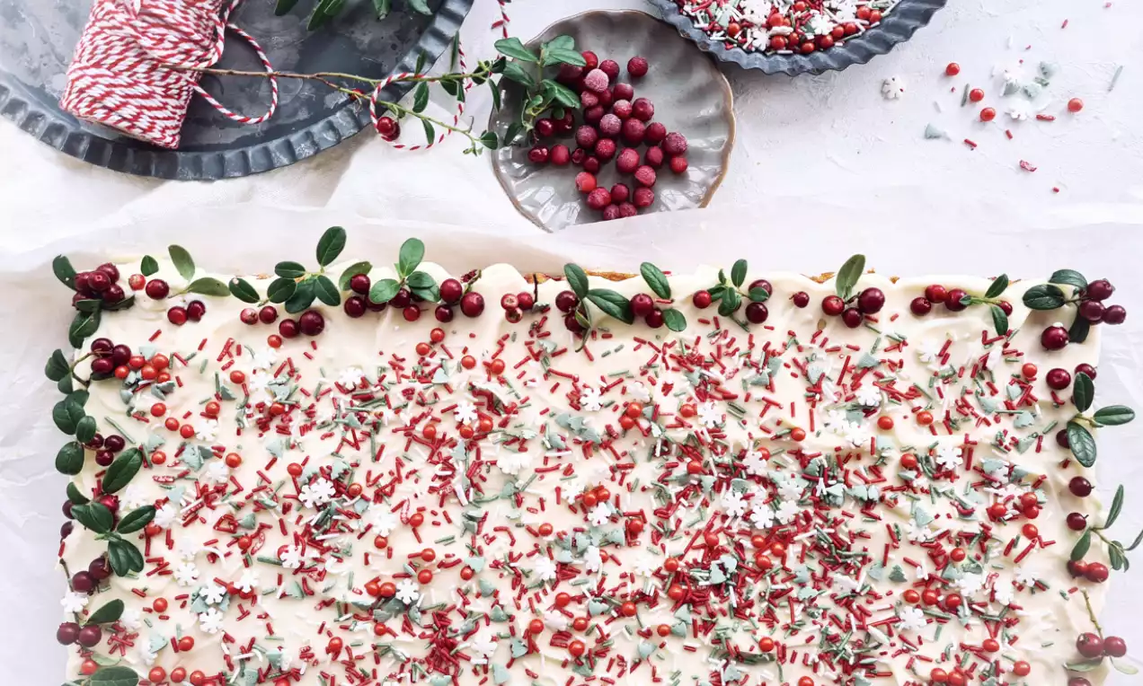 Kardemummarutor med ljus glasyr täckta av röda lingon och grön strössel, dekorerade med lingonkvistar på ett ljust underlag