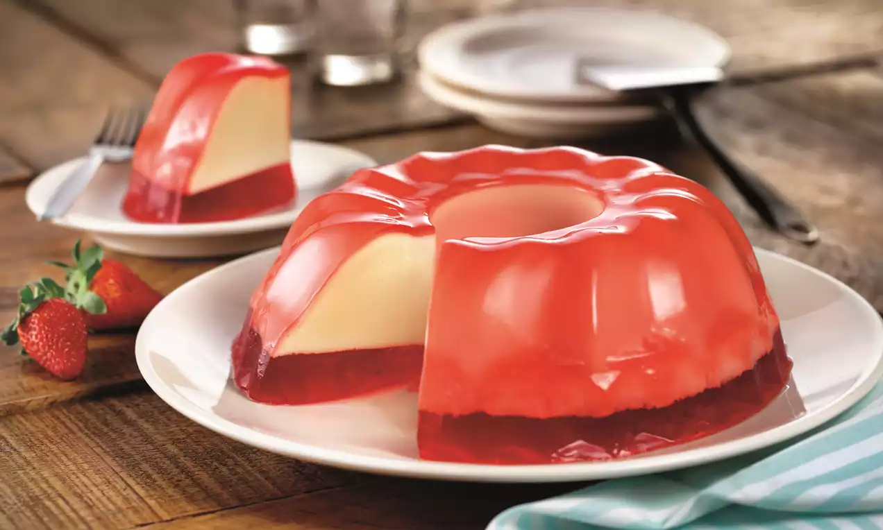 Gelatina recheada em camadas translúcidas rosa e branca com pedaços de morango e abacaxi e folhas de hortelã em prato branco