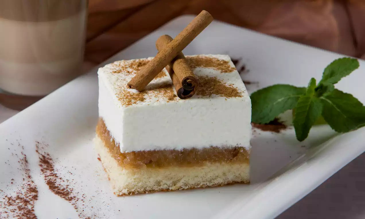 Kanadský jablkový koláč s vrstvou bieleho šľahačkového krému, zlatistého jablkového kompótu a piškótového základu, ozdobený škoricou a lístkami mäty